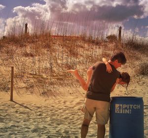 Rear view of playful father carrying daughter by garbage bin at sandy beach