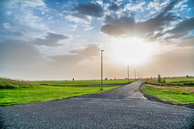 Empty road amidst field against sky