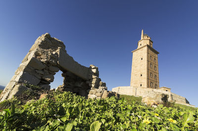 Tower of hercules on field against clear blue sky