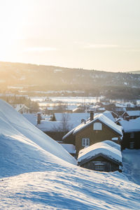 Snow covered houses by buildings against sky during winter