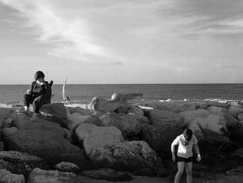 Woman looking at son while sitting on rock against sky