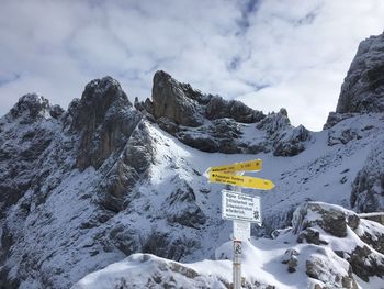 Road sign on snow covered mountain against sky