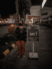 Woman standing by text on footpath at night