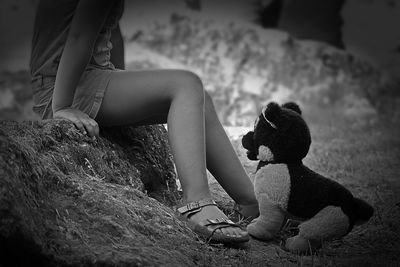 Low section of girl sitting by stuffed toy on field