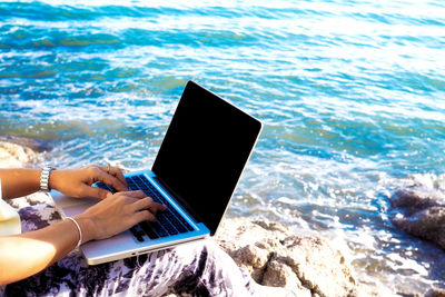 Midsection of woman using laptop at beach