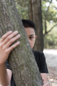 Portrait of teenage girl holding tree trunk