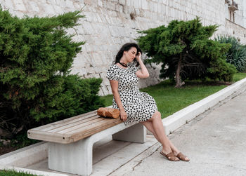 Portrait of attractive young woman in summer polka-dot dress sitting on bench.