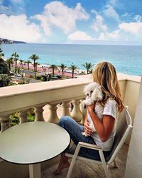 Woman with dog sitting on chair by sea against sky