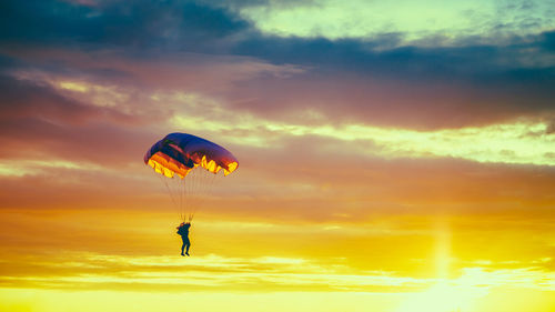 Low angle view of person paragliding against sky during sunset