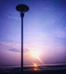 Street light by sea against sky during sunset