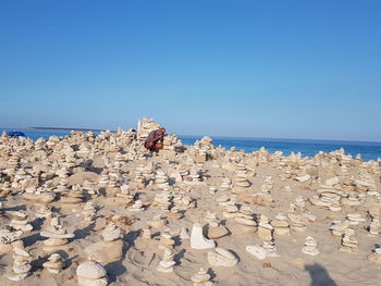 Mature man crouching on rocky beach against clear blue sky during sunny day