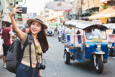 Portrait of smiling young woman using smart phone on street