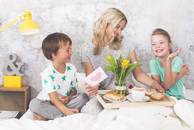 Cheerful mother with children having breakfast on bed