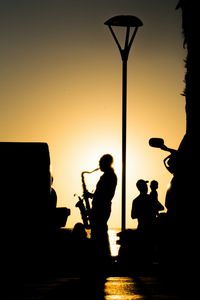 Silhouette people playing at music concert against sky during sunset