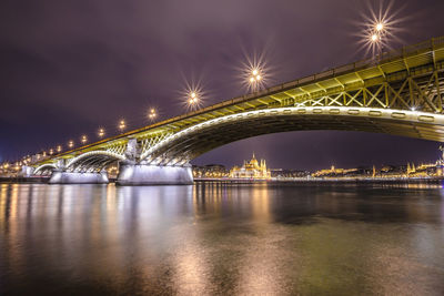 Illuminated arch bridge over river against sky at night