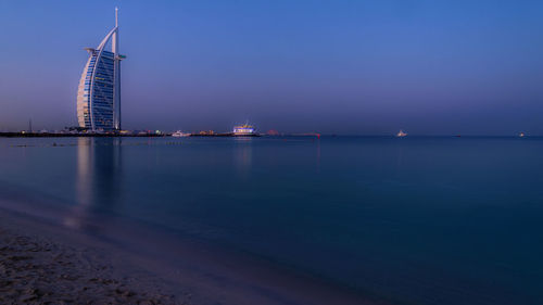 Burj al arab by sea against sky during sunrise in city