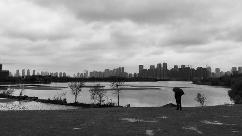 Rear view of man standing on riverbank against cloudy sky