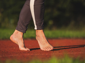 Barefoot woman walks on tiptoe, stretching tendons and ankles on red running track in long leggings
