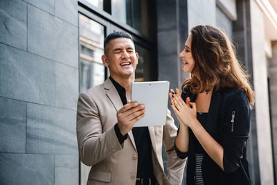 Young couple holding smart phone while standing on wall