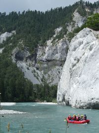 Rear view of people river rafting by rocky mountains