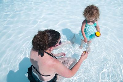 High angle view of mother and daughter in swimming pool on sunny day