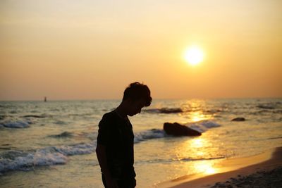 Man standing on beach against sky during sunset