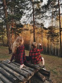 Rear view of people sitting on wood in forest