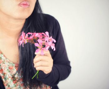 Close-up of woman holding pink flowers against wall