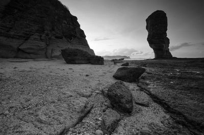 Rear view of rock formation on beach against sky