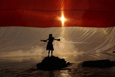 Rear view of silhouette man standing on rock at sea