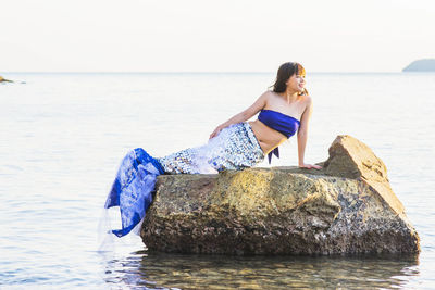 Young woman on rock at beach against sky