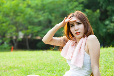 Woman shielding eyes while sitting on field