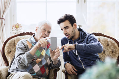 Caretaker assisting elderly man in using mobile phone at nursing home