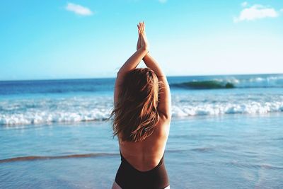 Rear view of woman standing at beach against sky