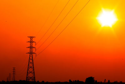 Silhouette electricity pylon against orange sky