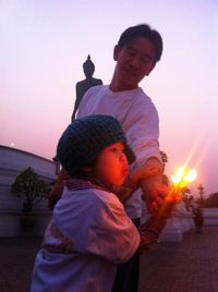 Full length of father with son against sky during sunset