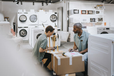 Multiracial male and female coworkers discussing over calculator while working in appliances store