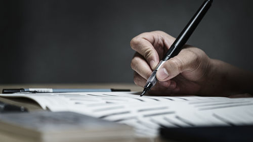 Close-up of hand holding paper with pen on table