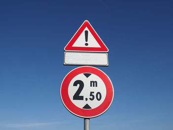 Low angle view of road sign against clear blue sky