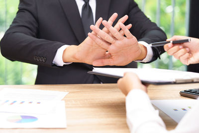 Cropped hands of person giving documents and pen to sign while man refusing over table