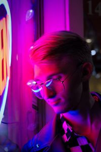 Close-up young man wearing eyeglasses standing by illuminated store