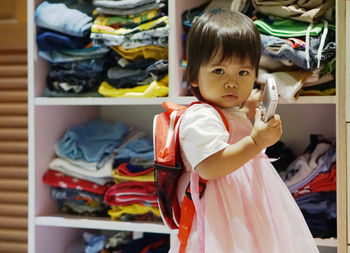 Portrait of cute girl with toy standing against shelf at home