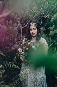 Portrait of young woman standing by tree in forest