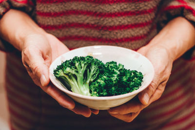 The midsection of senior woman holding steamed broccoli in the bowl. / housewife / cooking at home