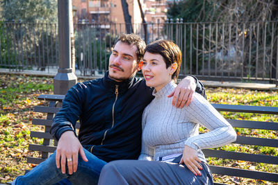 Young couple is sitting on a bench in the park in rome. couple is embracing themselves in the park.