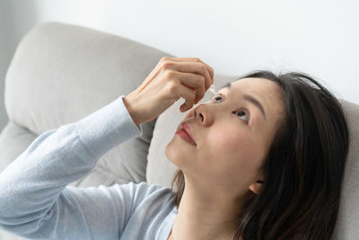 Woman putting eye drop sitting on sofa at home