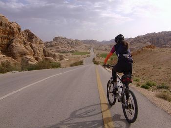 Woman riding bicycle on road against sky