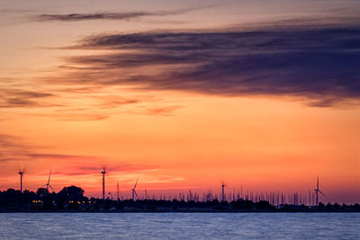 Silhouette sailboats in sea against dramatic sky during sunset