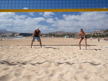 Full length of men playing on beach against sky