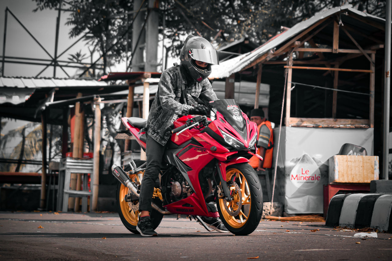 MAN RIDING MOTORCYCLE ON ROAD AGAINST BUILDINGS